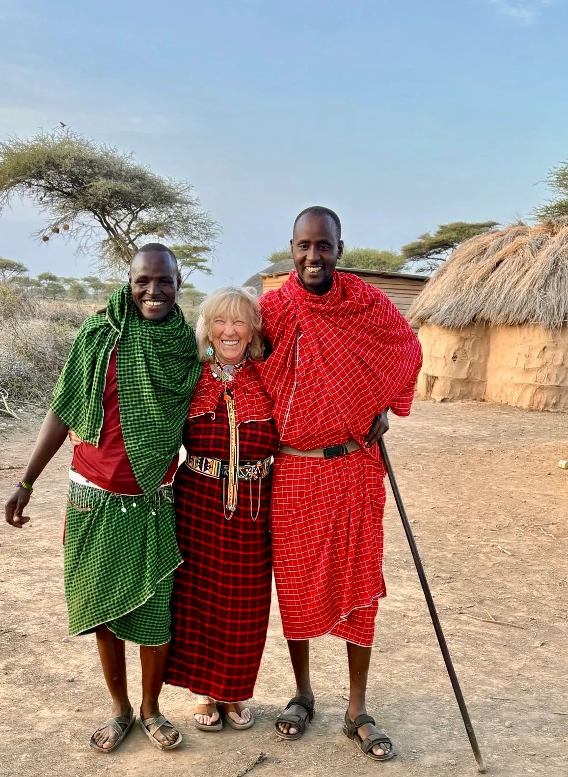 Three people smiling, traditional attire, rural setting.