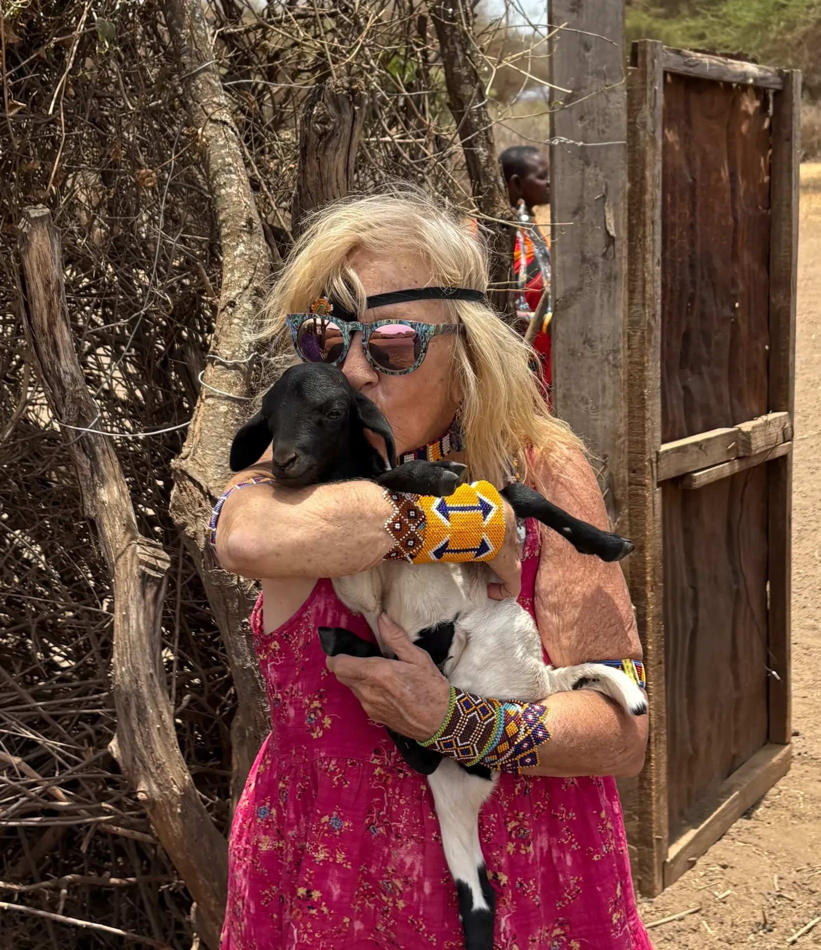 Woman hugging a goat near wooden gate.