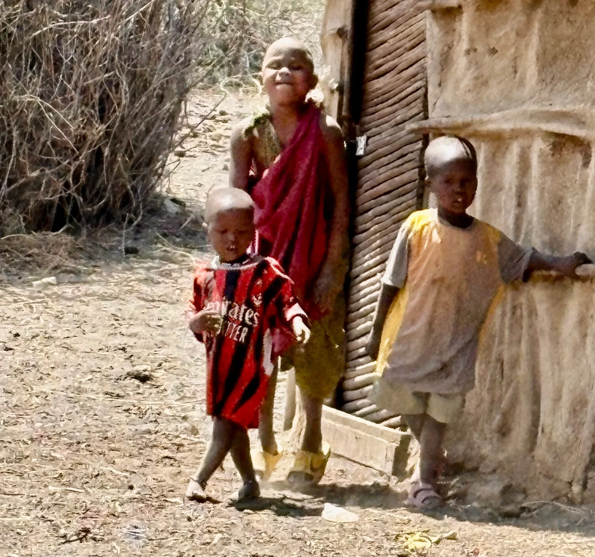 Three children standing outside a rustic building.