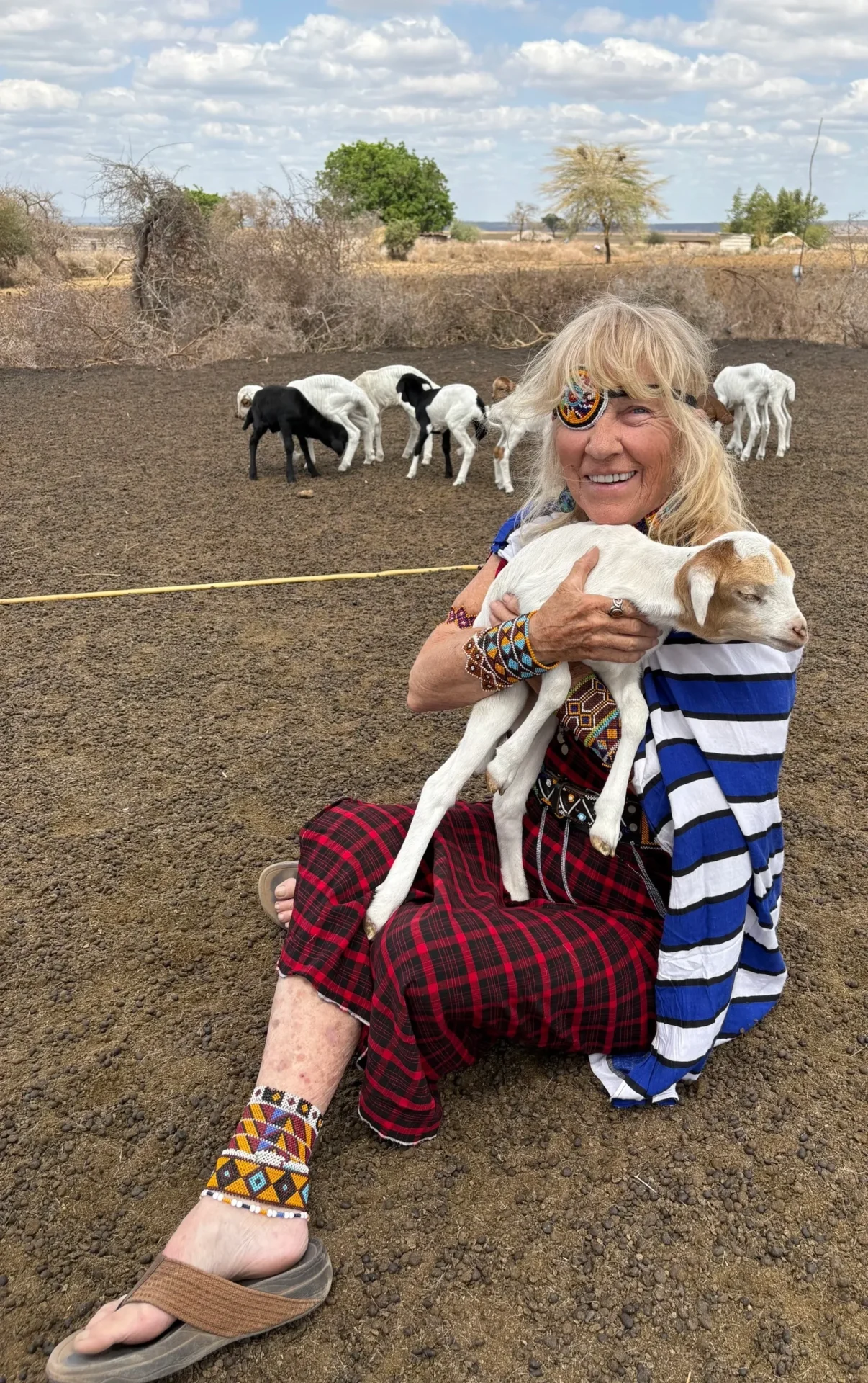 Woman holding goat, sitting on dirt ground.
