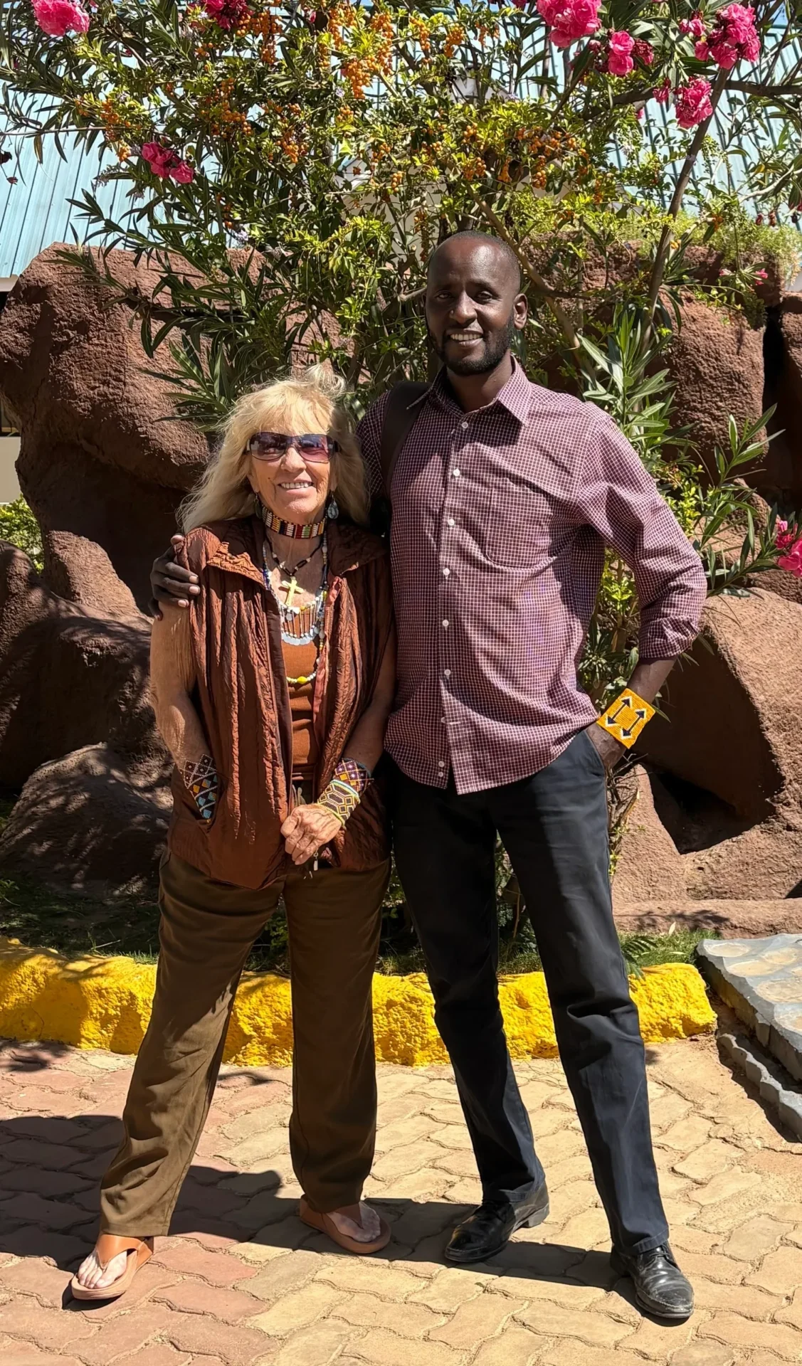 Two people posing by flowering bushes.