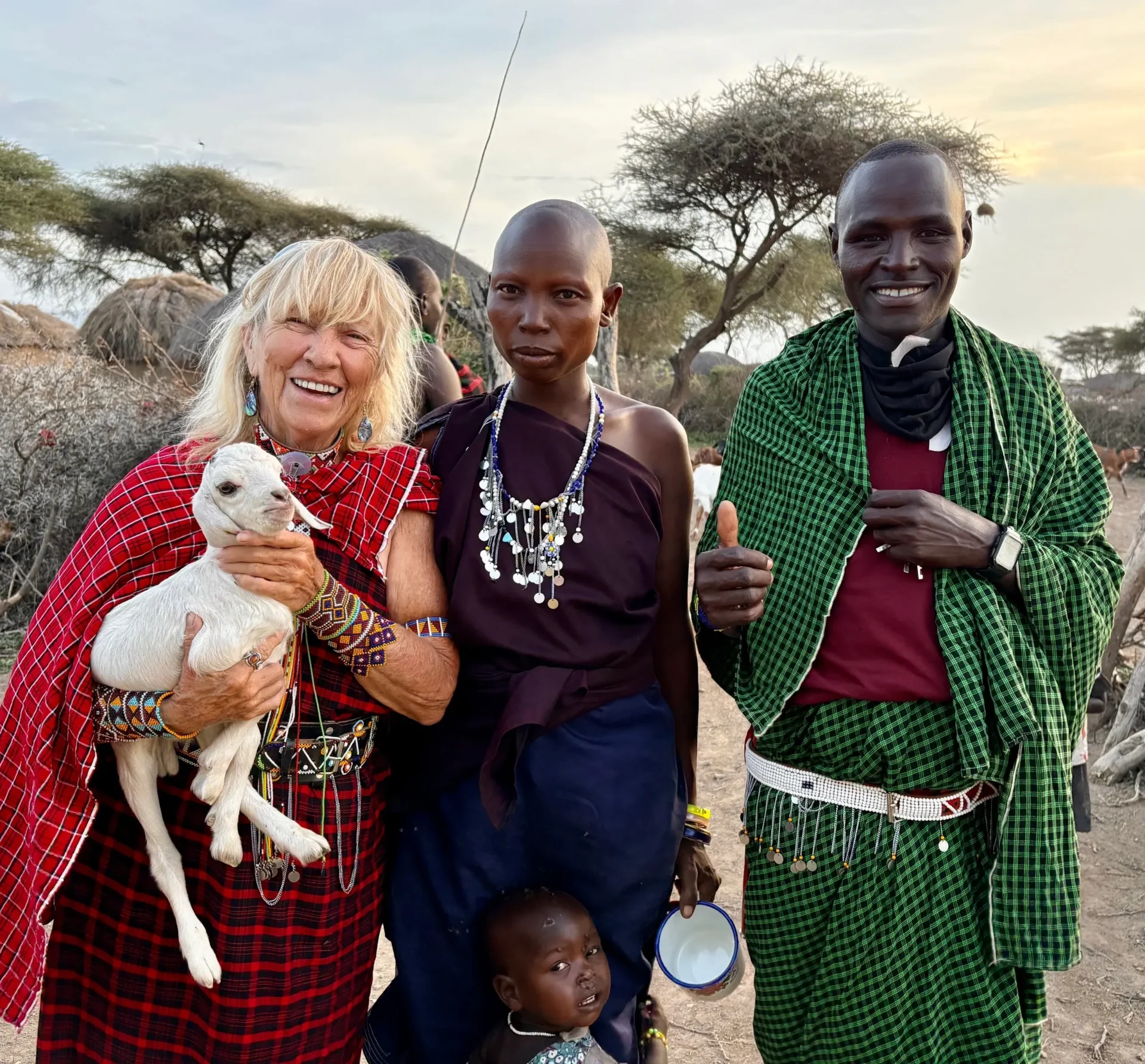 Group of people with goat, smiling outdoors.